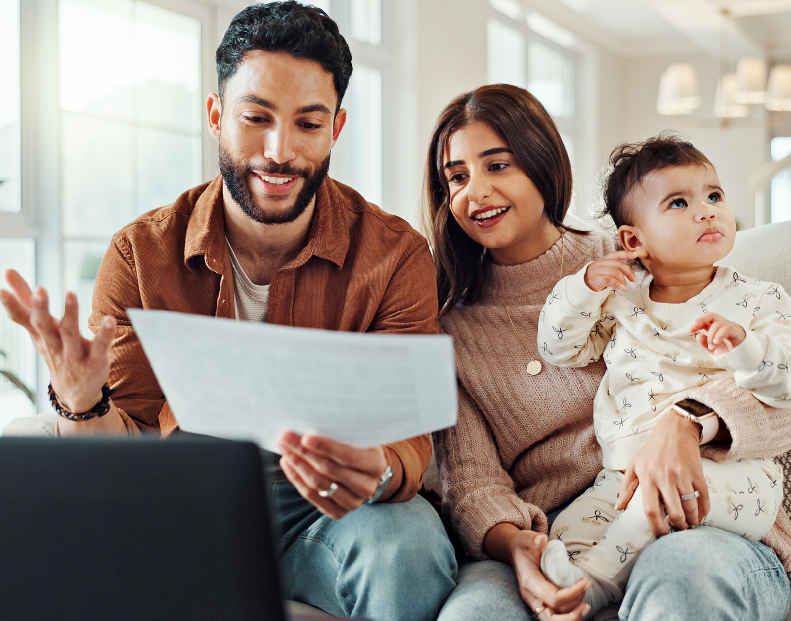 Smiling couple with their baby reviewing financial documents at home.