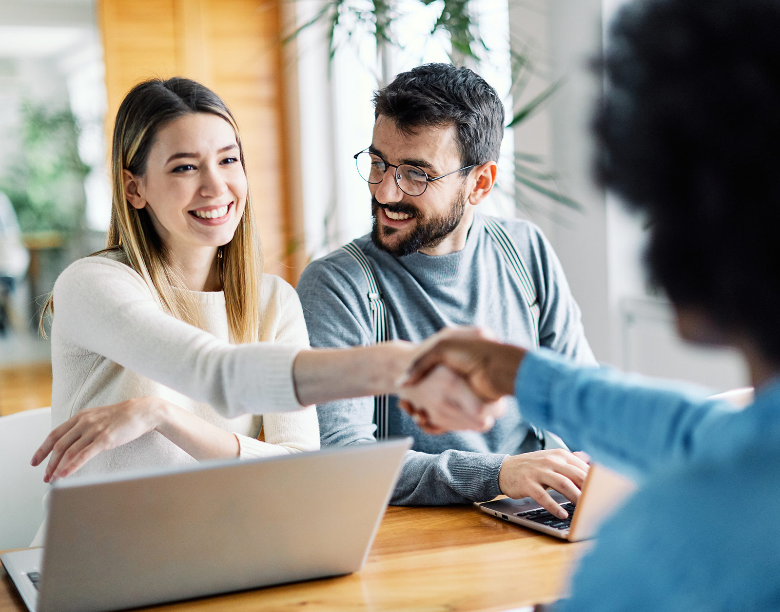 Two customers smiling and shaking hands with a banking professional during a meeting.